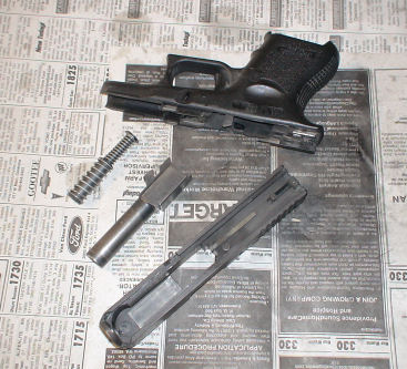 Disassembled Glock parts: (top) slide (bottom row left to right) recoil spring, barrel, slide.